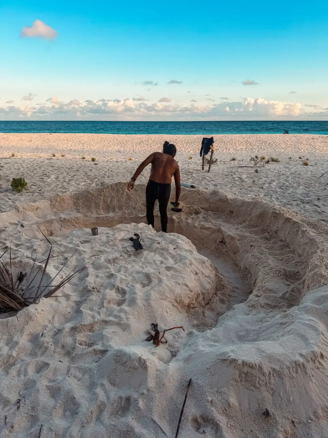 Man digging large hole on a white sand beach in the Maldives. Turquoise sea, blue sky.