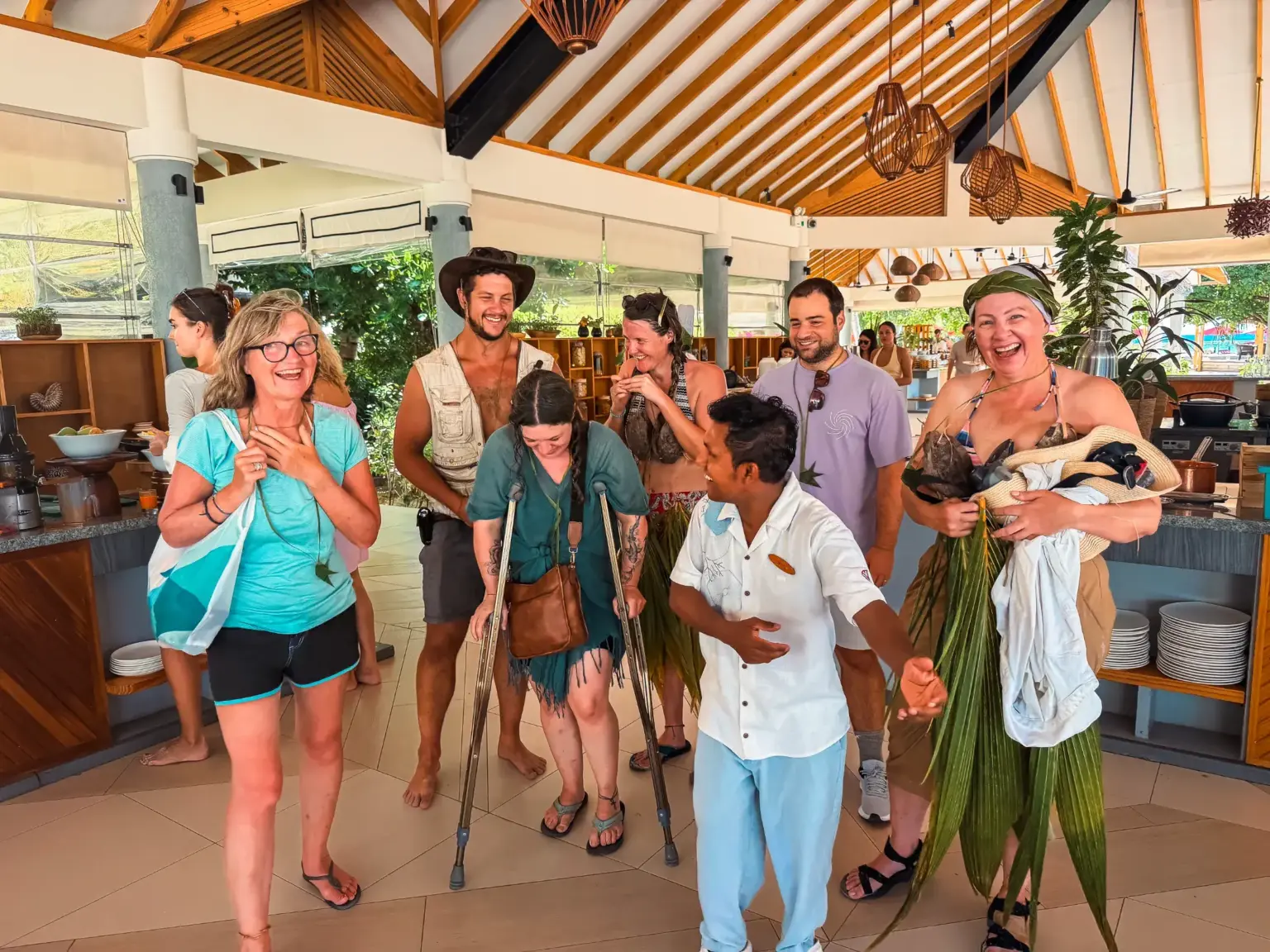 Group in Maldives, one on crutches, laughs with resort staff. Survival in the Maldives theme.