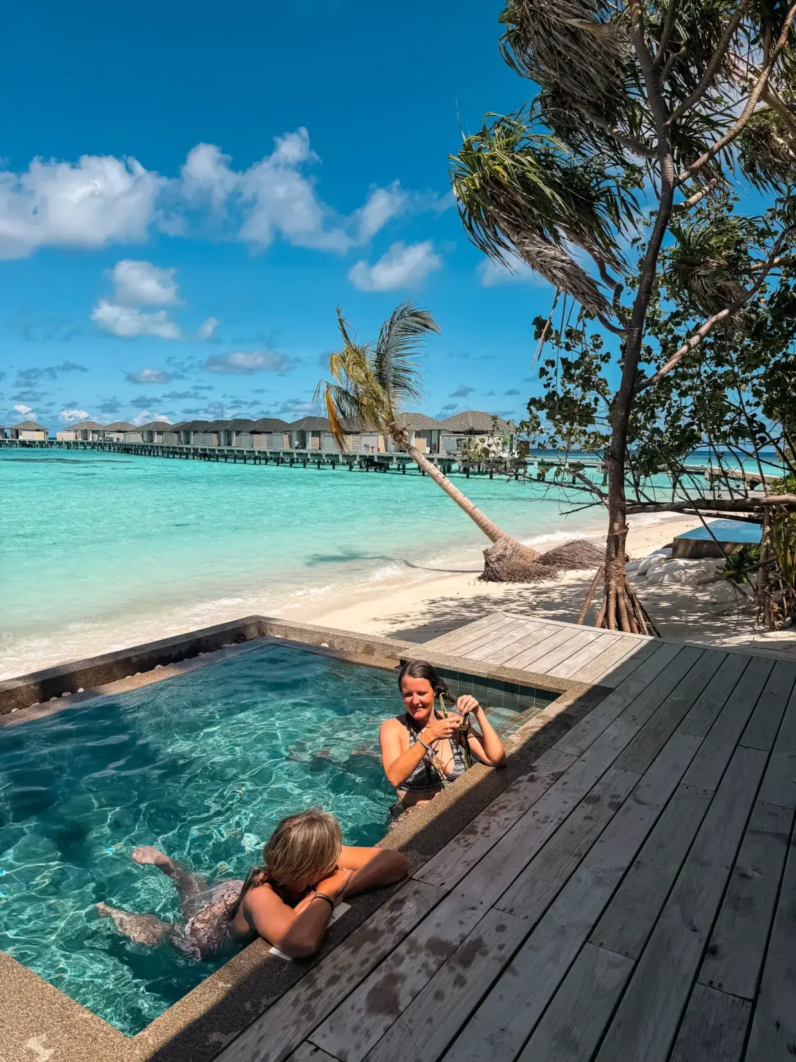 Two women relaxing in a private pool at a Maldives resort with overwater bungalows.