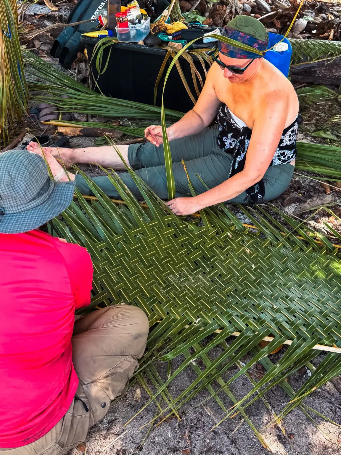 People weaving palm fronds on a beach, possibly for survival in the Maldives.