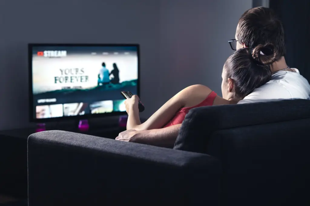 Couple watching TV at home, embracing on couch. Streaming service displayed on screen.