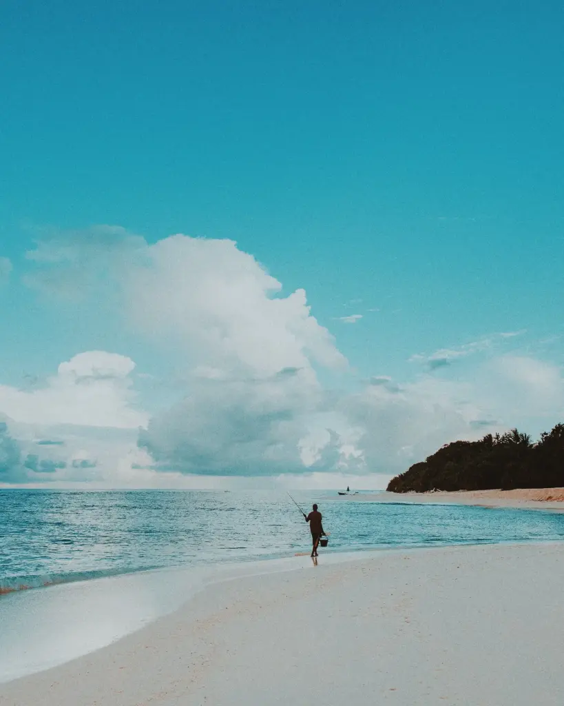 Fisherman walking on beach, blue sky and ocean, tropical island backdrop.