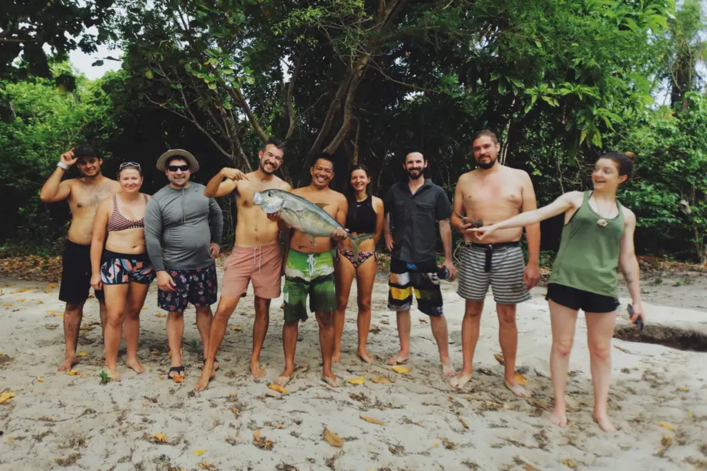 Group of people on a beach holding a large fish, smiling.