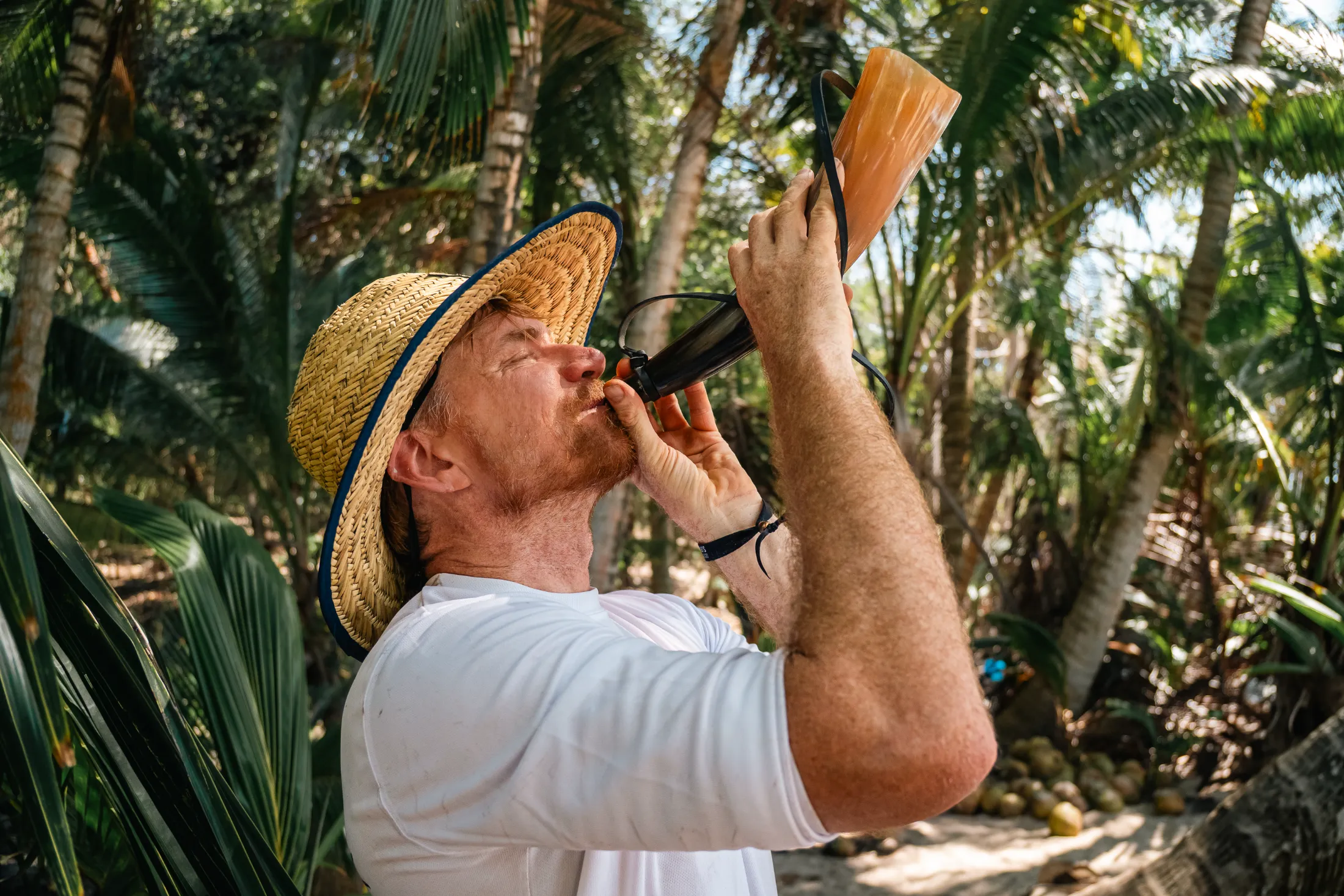 Man drinking from horn in tropical jungle, desert island survival training.