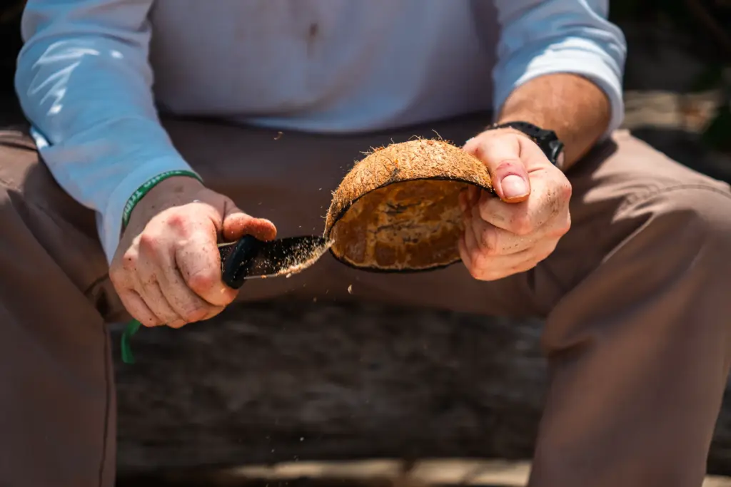 Man opening coconut with knife, desert island survival training.