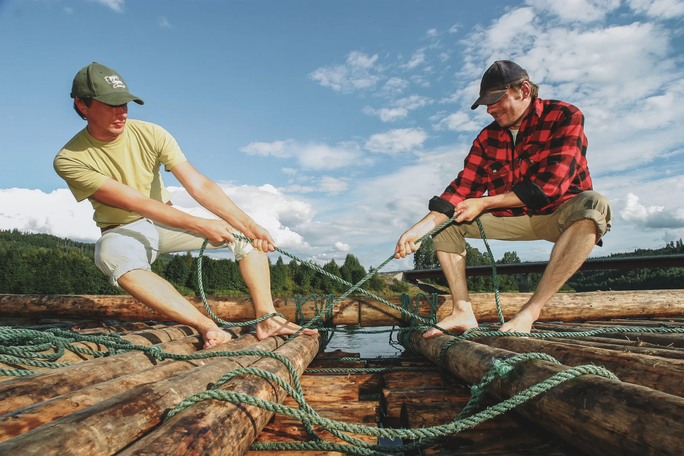Two men building a raft, pulling ropes on a log raft on a lake.