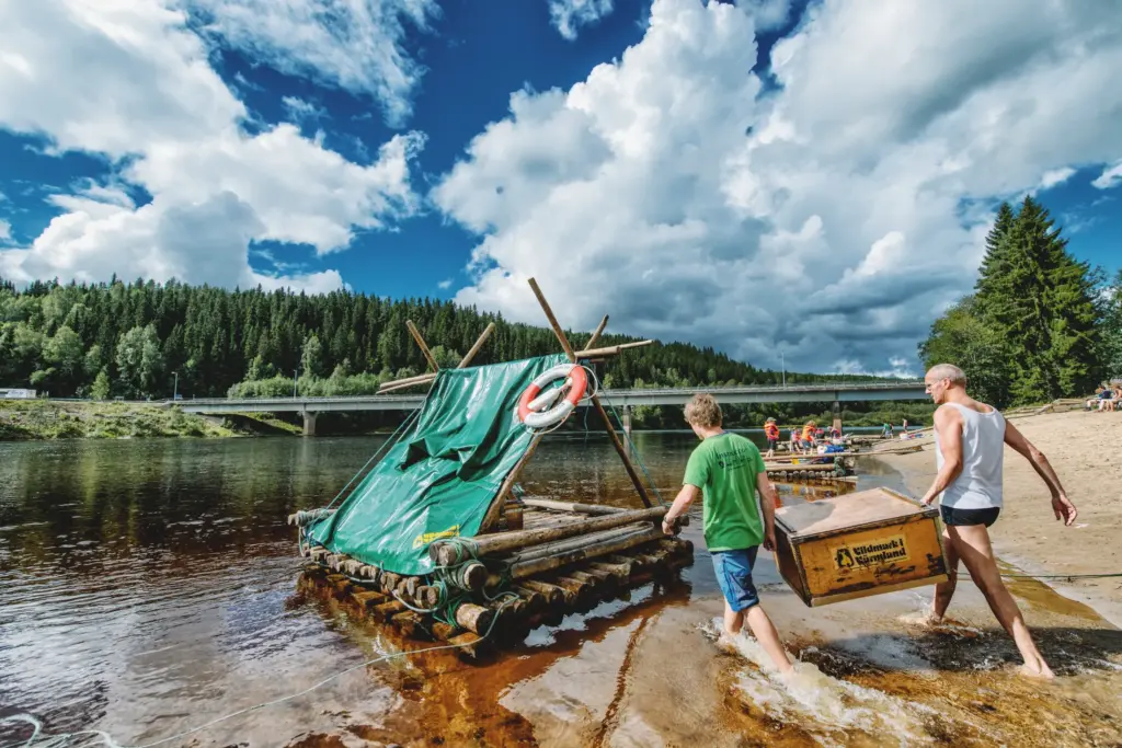 Men pulling a raft ashore with a wooden box, river adventure.