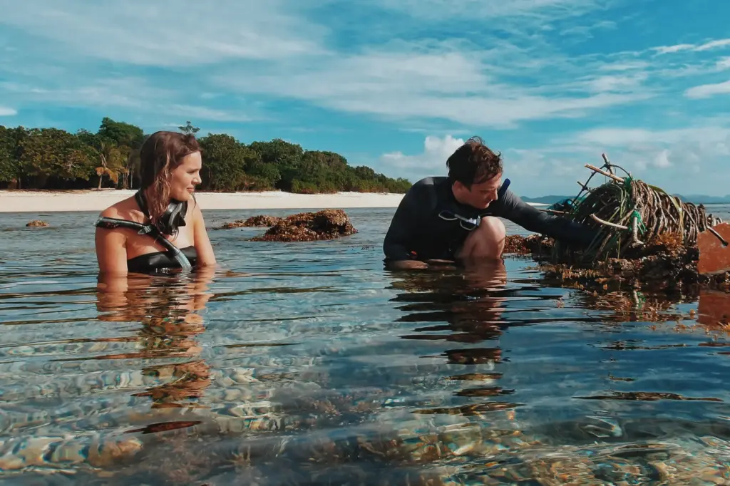 Survival training: Woman and man examining debris in shallow tropical water.