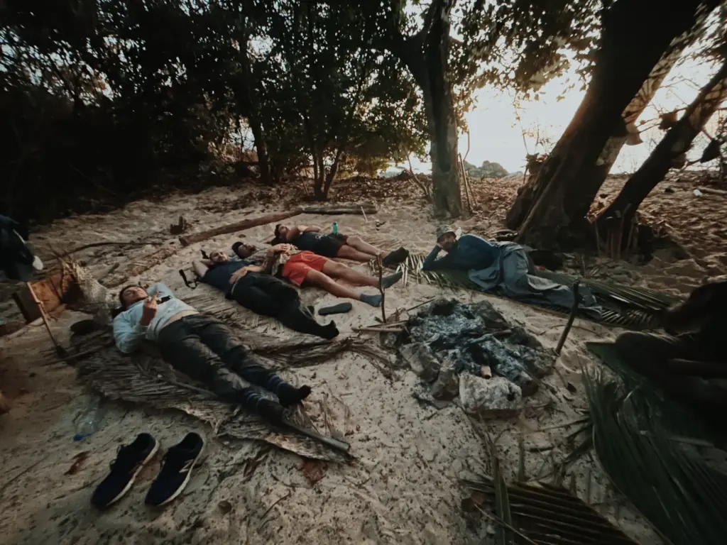 Survival training group resting on beach after camp, under trees.