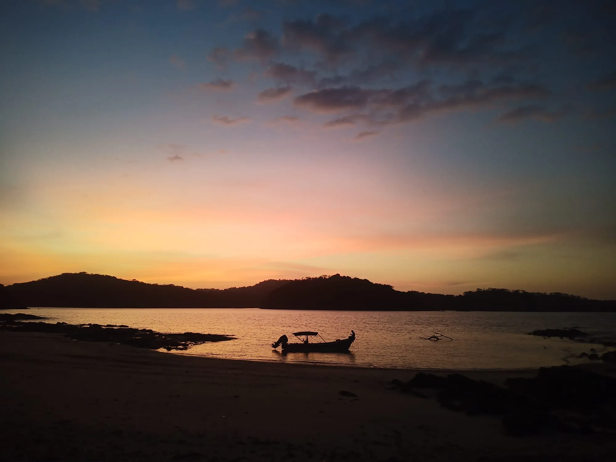 Sunset over tropical island bay with a small boat on the water.