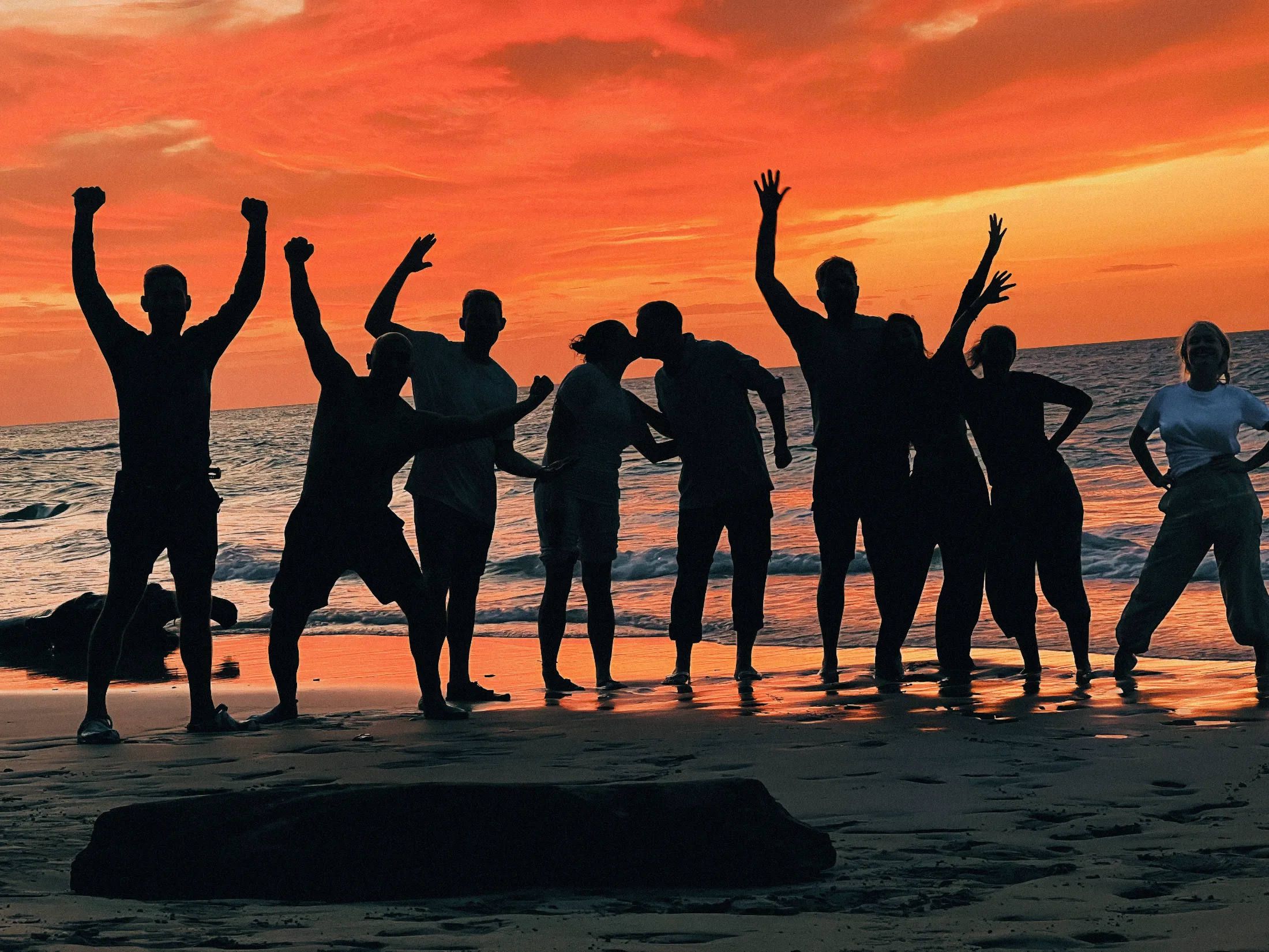 Silhouettes of a group of people celebrating on a beach at sunset