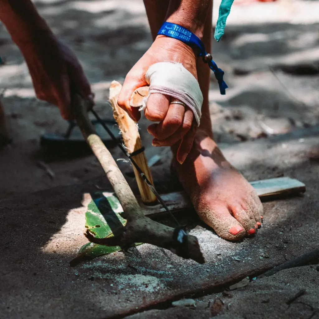 Hands using bow drill to start fire, survival skills, Desert Island Survival bracelet visible.