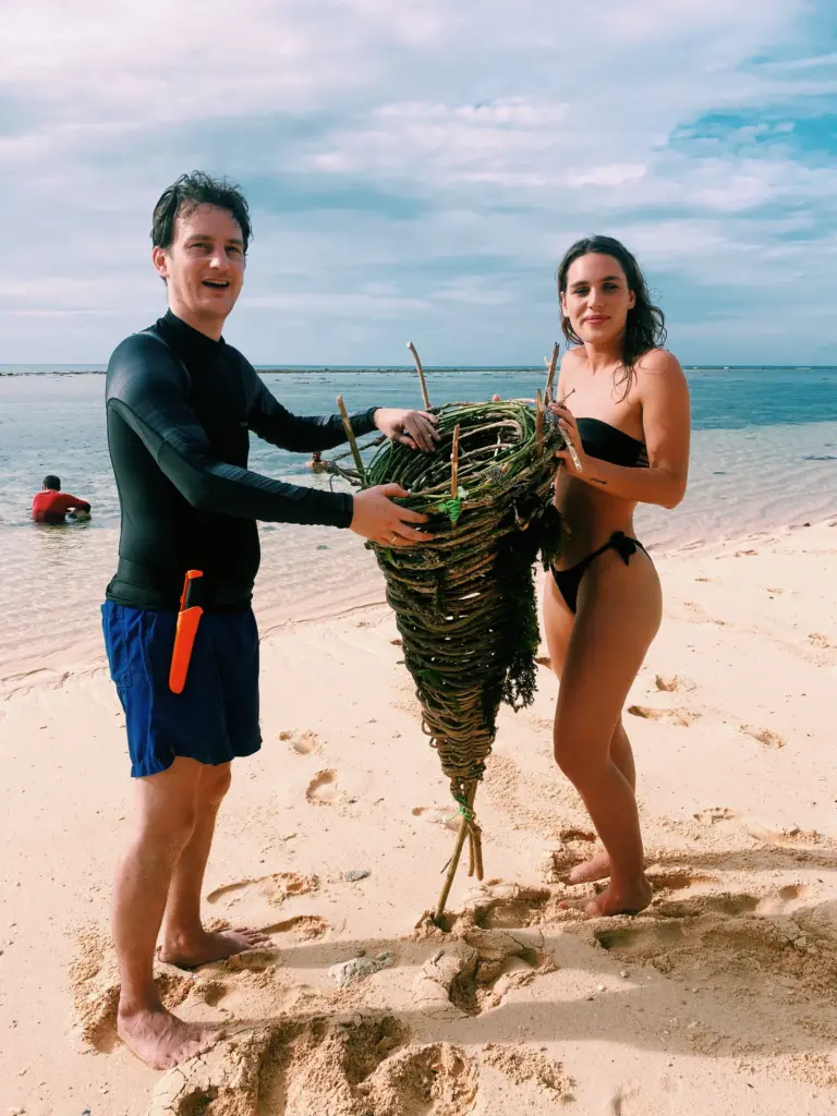Couple holding handmade survival shelter on beach, survival expedition.