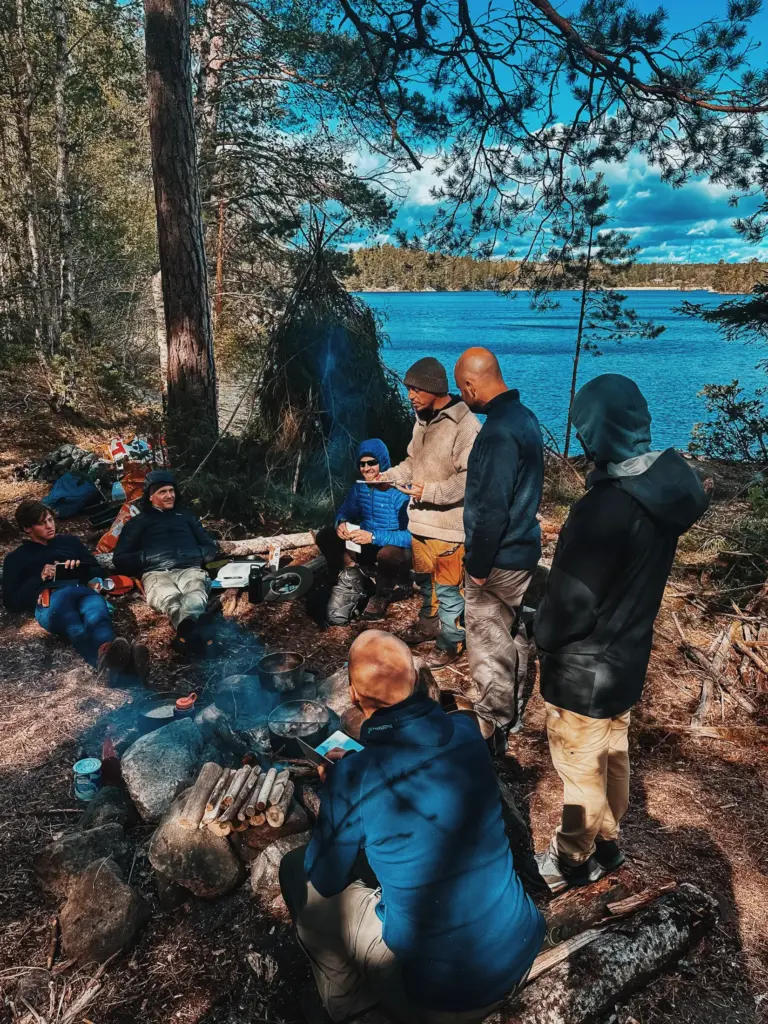 Group camping by lake in Sweden, gathering around campfire for wilderness adventure.