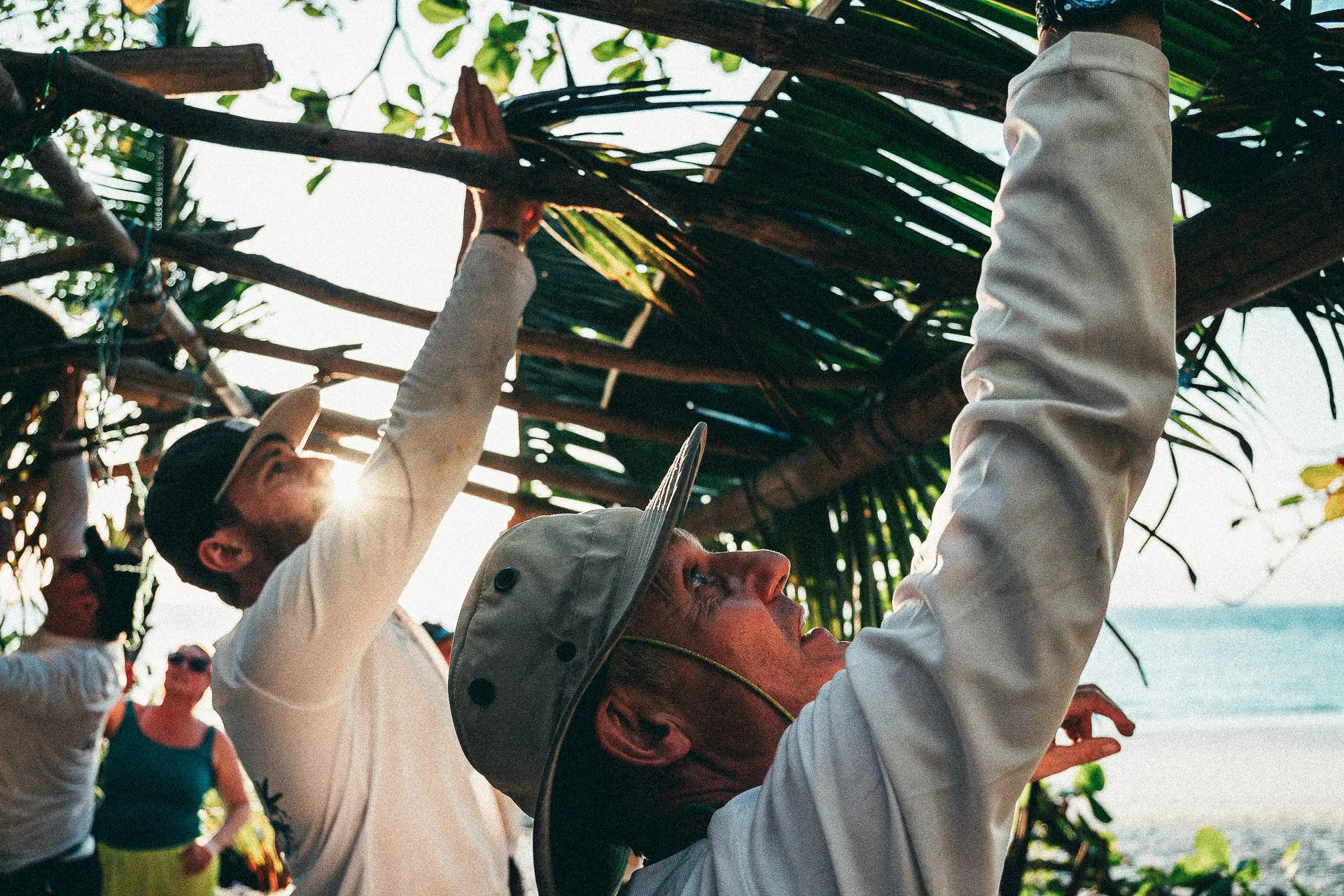 Expedition team members fixing roof of shelter on beach with ocean in background
