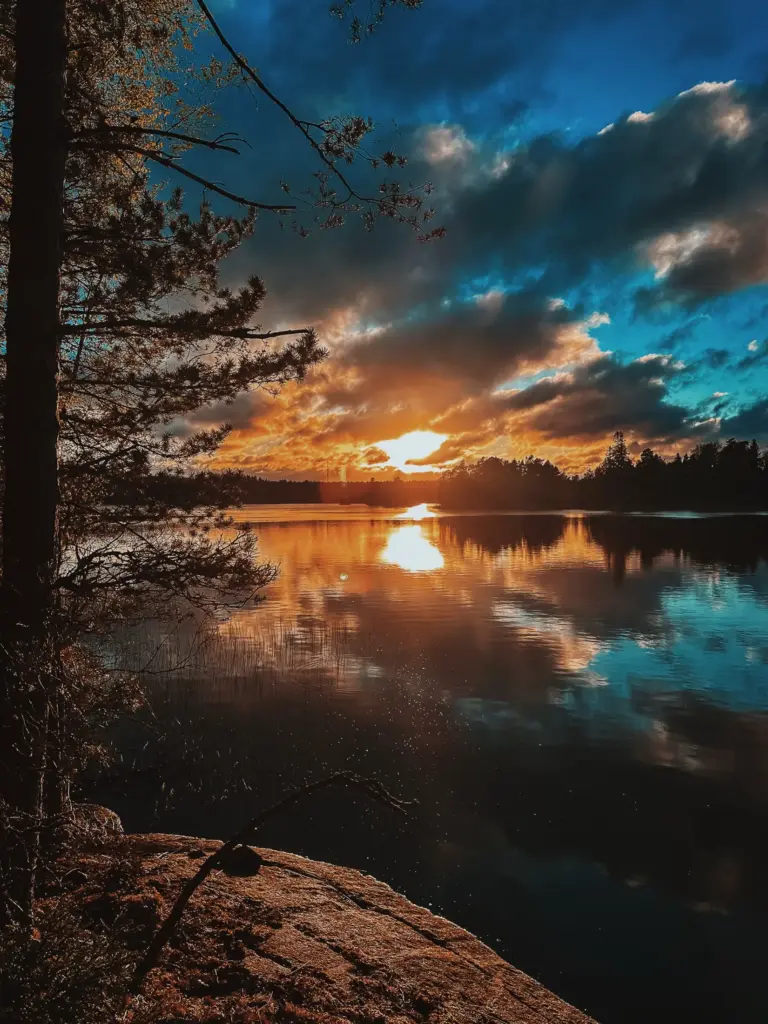 Sunset over calm lake in Sweden with trees, reflecting golden light and blue sky. Wilderness scene.