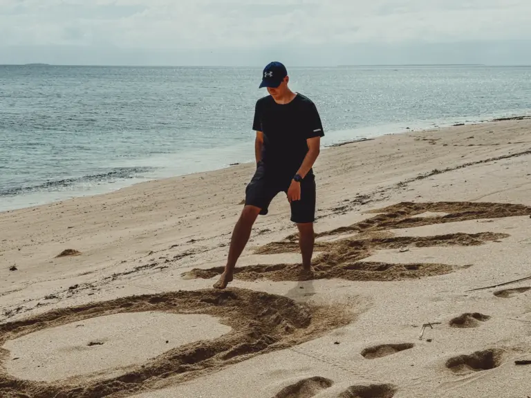 Man drawing in sand on a beach with ocean in background