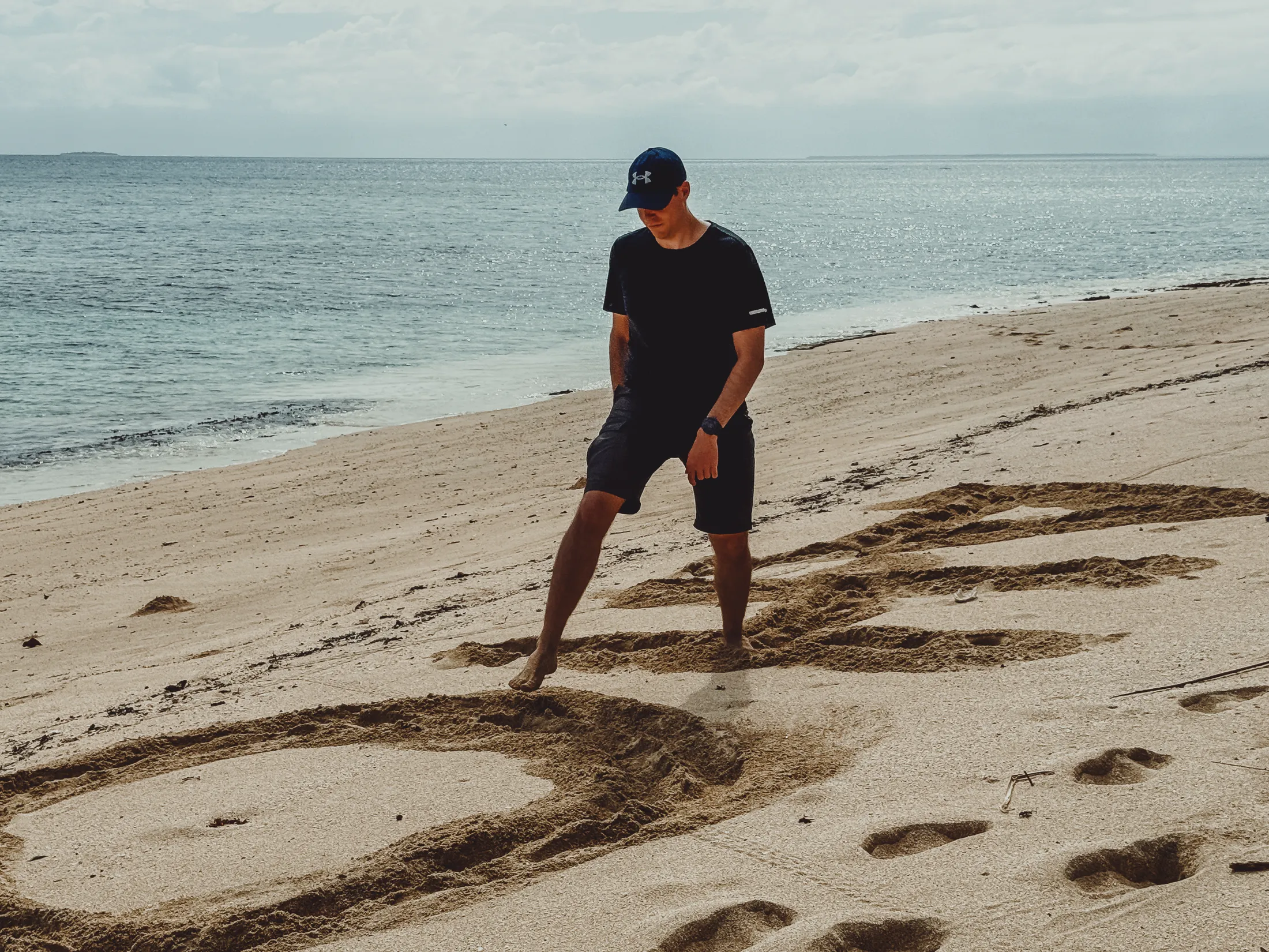 Man drawing in sand on a beach with ocean in background