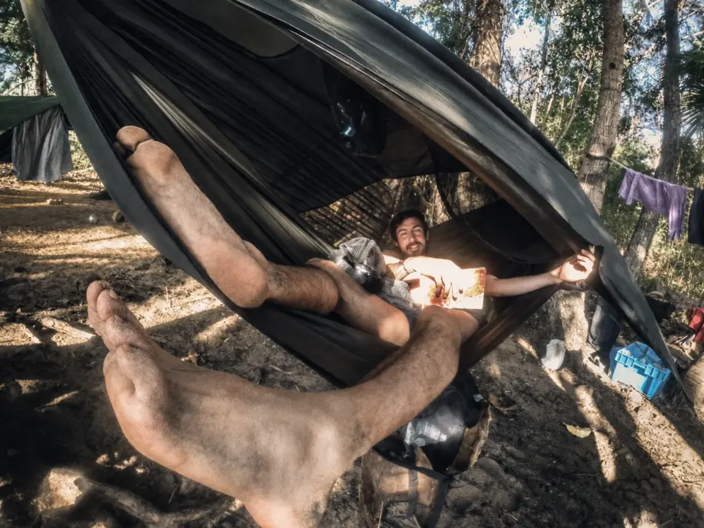 Man relaxing in a hammock in a forest setting, with his feet visible in the foreground.